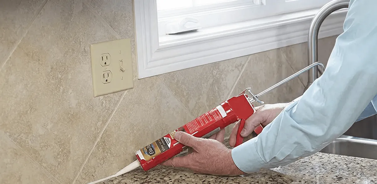 Handyman applying caulk along a kitchen backsplash and countertop seam in Rockford, IL