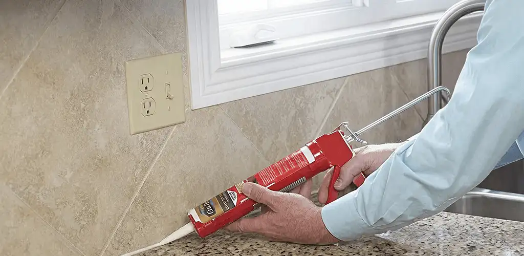 Handyman applying caulk along a kitchen backsplash and countertop seam in Rockford, IL