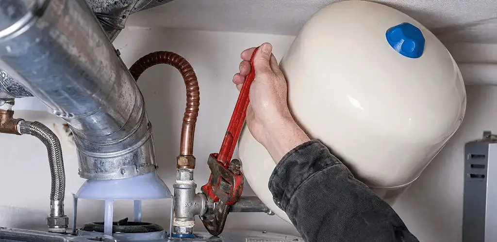 Water heater repair technician tightening plumbing connections near a tank unit in Rockford, IL